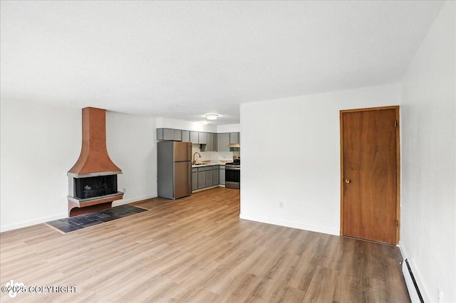 933 W 20th Ave, Anchorage, AK 99503 - unfurnished living room featuring light wood-style flooring, a baseboard radiator, and a wood stove