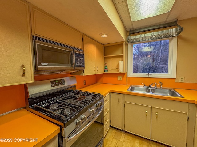 kitchen featuring gas range, black microwave, a sink, light countertops, and light wood finished floors