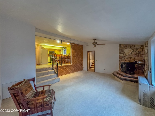 carpeted living room featuring stairs, a wood stove, a ceiling fan, and wood walls