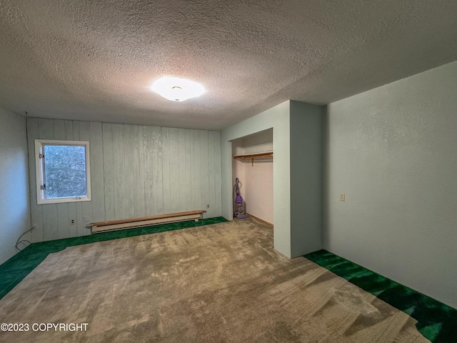 unfurnished bedroom featuring baseboard heating, carpet floors, a textured ceiling, wood walls, and a closet