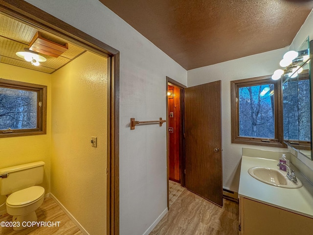 bathroom featuring wood finished floors, vanity, toilet, a textured wall, and baseboards