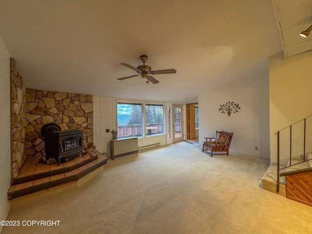 unfurnished living room with a wood stove, a baseboard radiator, ceiling fan, and carpet