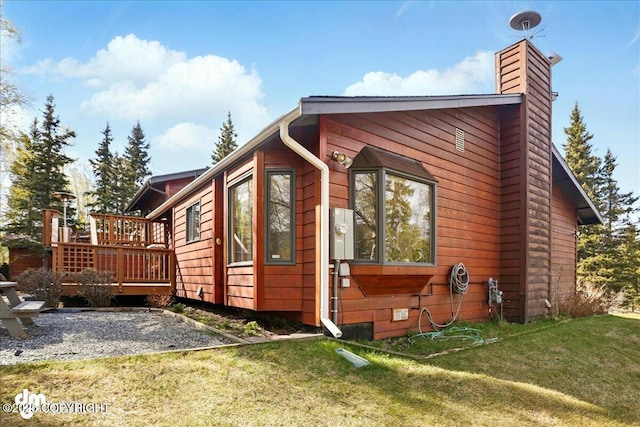 view of side of property featuring a deck, a lawn, and a chimney