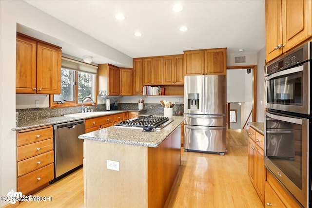 kitchen with stainless steel appliances, a sink, light wood-style flooring, light stone countertops, and a kitchen island