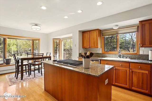 kitchen with a sink, a kitchen island, light wood finished floors, stainless steel gas cooktop, and dark stone countertops