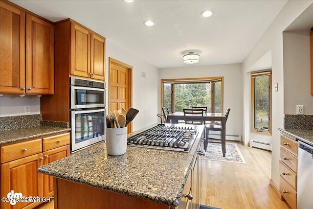 kitchen with a baseboard heating unit, stainless steel appliances, light wood-type flooring, dark stone countertops, and recessed lighting