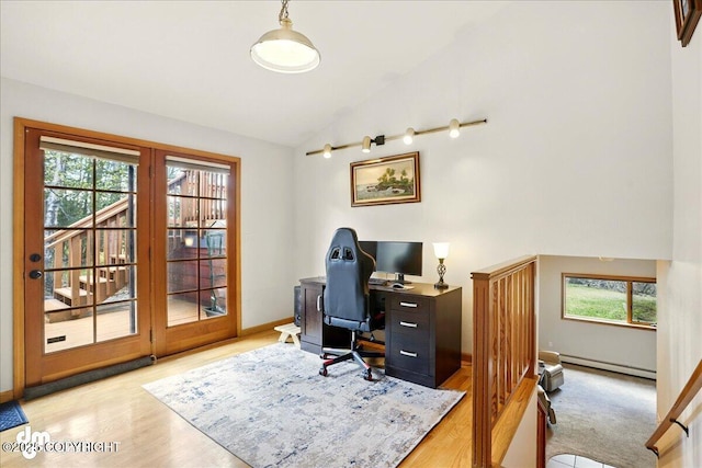 home office with lofted ceiling, a baseboard heating unit, light wood-style floors, and baseboards