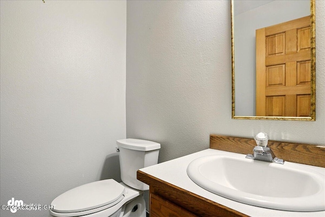 half bath with vanity, toilet, and a textured wall
