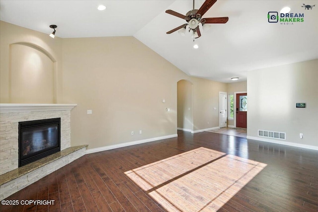 7782 W Arlie Rd, Wasilla, AK 99623 - unfurnished living room featuring ceiling fan, arched walkways, wood finished floors, a fireplace, and vaulted ceiling