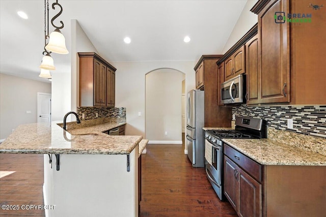 7782 W Arlie Rd, Wasilla, AK 99623 - kitchen featuring stainless steel appliances, dark wood-type flooring, backsplash, a peninsula, and arched walkways