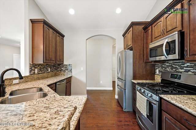 7782 W Arlie Rd, Wasilla, AK 99623 - kitchen featuring stainless steel appliances, dark wood finished floors, light stone counters, arched walkways, and tasteful backsplash