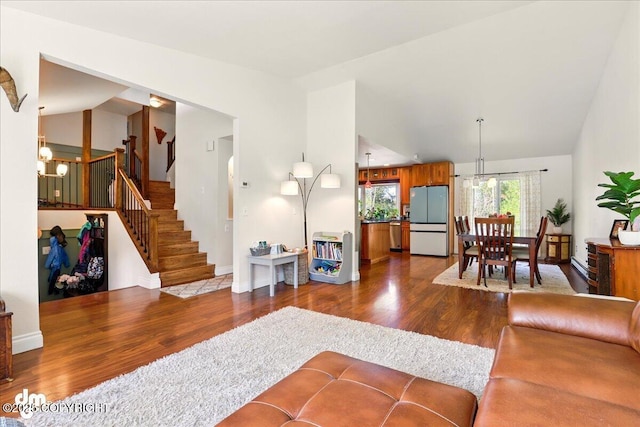 living area featuring a chandelier, lofted ceiling, dark wood finished floors, stairs, and baseboards