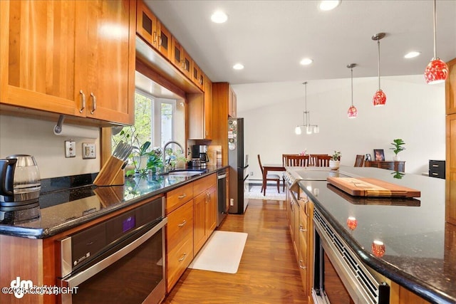 kitchen with stainless steel appliances, a sink, wood finished floors, brown cabinetry, and recessed lighting