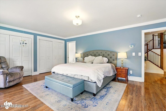 bedroom featuring baseboards, two closets, wood finished floors, and crown molding