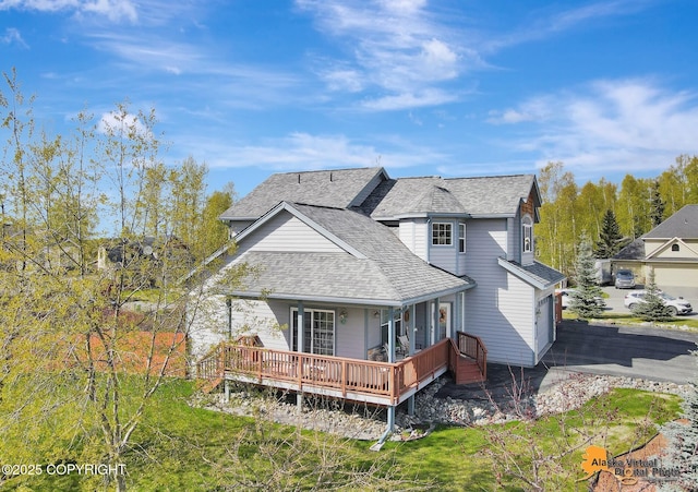rear view of property featuring driveway, a shingled roof, and a garage