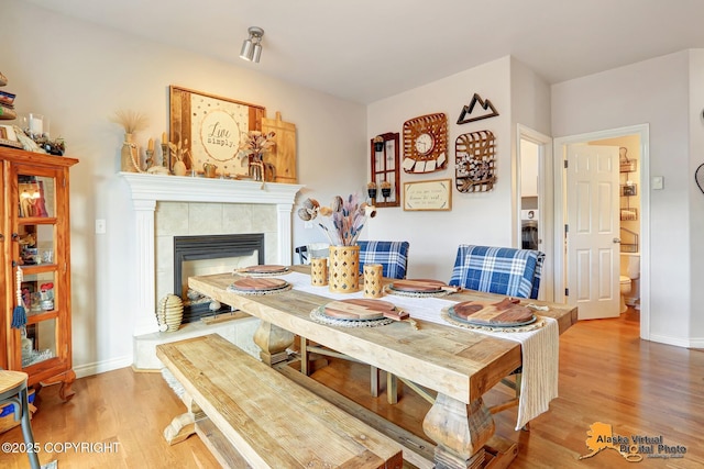 dining room with wood finished floors, a tiled fireplace, and baseboards