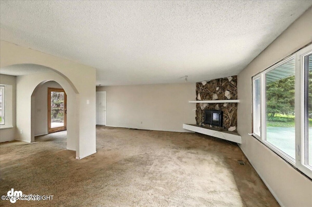 unfurnished living room with carpet flooring, arched walkways, plenty of natural light, a textured ceiling, and a fireplace