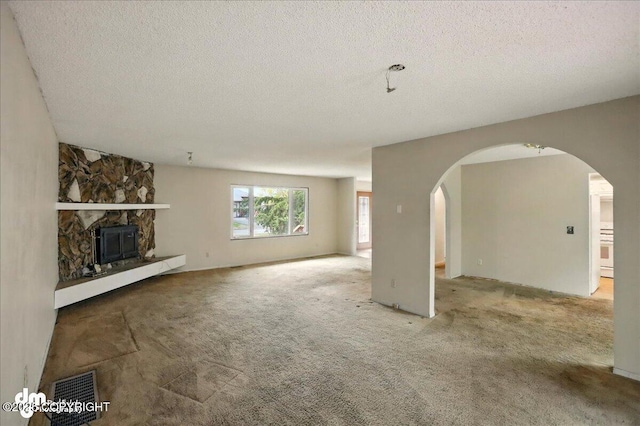 unfurnished living room with arched walkways, a textured ceiling, carpet floors, and a stone fireplace