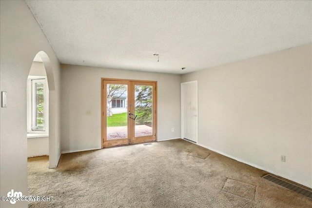 carpeted empty room featuring arched walkways, french doors, a textured ceiling, and baseboards