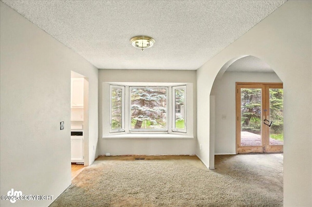 carpeted empty room featuring healthy amount of natural light, arched walkways, a textured ceiling, and french doors