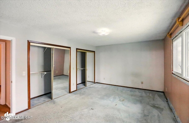 unfurnished bedroom with two closets, light colored carpet, a textured ceiling, and baseboards