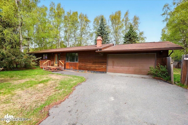 view of front of property featuring an attached garage, a chimney, asphalt driveway, and a front lawn