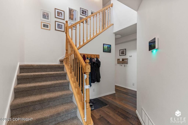 staircase featuring wood finished floors, baseboards, and a towering ceiling