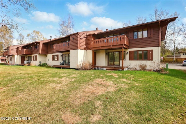 back of property featuring a balcony, a yard, and stucco siding