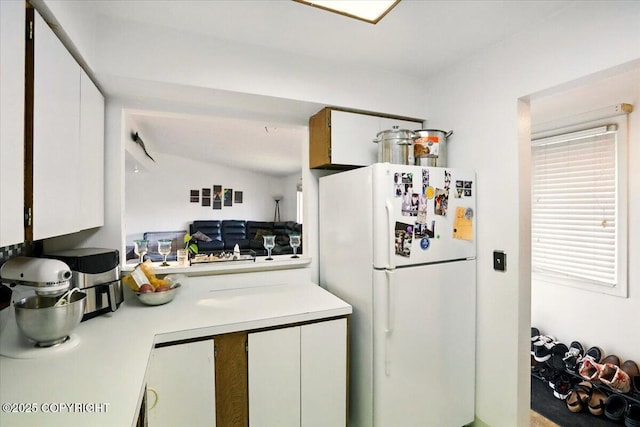 kitchen with freestanding refrigerator, light countertops, white cabinets, and lofted ceiling