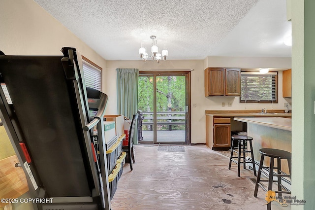 kitchen featuring freestanding refrigerator, a textured ceiling, a chandelier, light countertops, and brown cabinetry