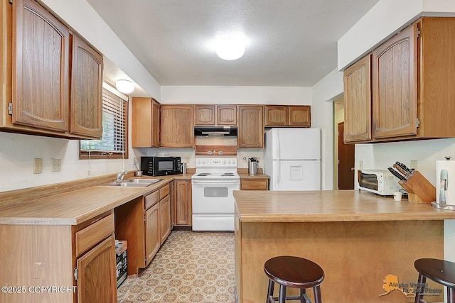 kitchen with white appliances, a peninsula, under cabinet range hood, and a kitchen bar