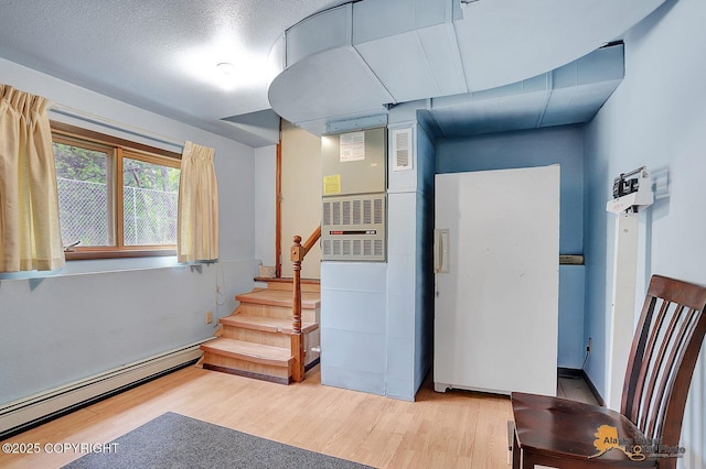 below grade area with light wood-style flooring, a baseboard radiator, and stairs