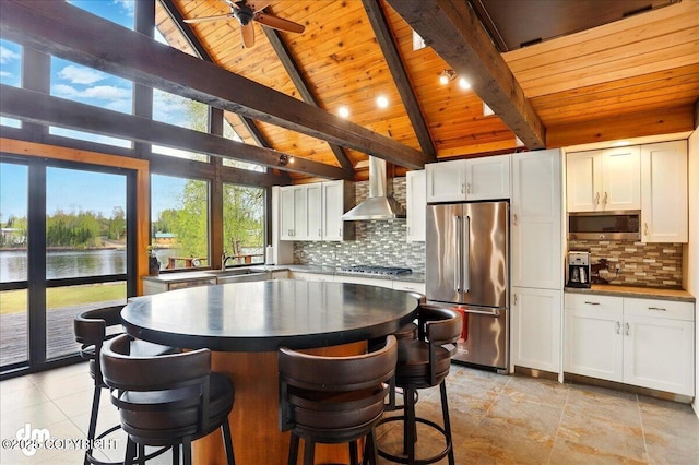 kitchen with appliances with stainless steel finishes, wall chimney exhaust hood, wood ceiling, a water view, and white cabinetry