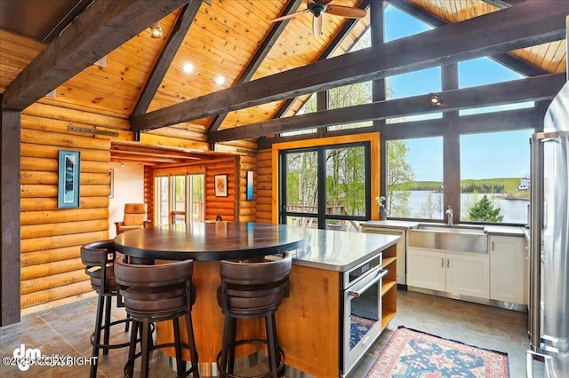 kitchen featuring wooden ceiling, oven, stainless steel counters, white cabinetry, and a sink