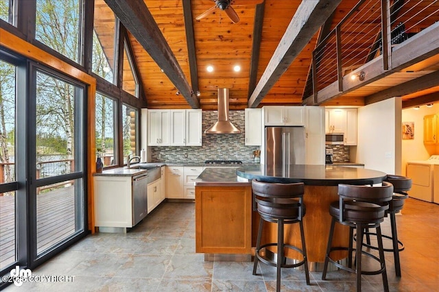 kitchen featuring wall chimney exhaust hood, stainless steel appliances, washer and dryer, wooden ceiling, and beamed ceiling
