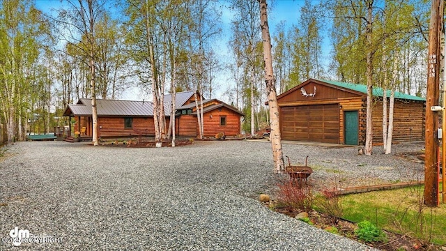 view of front of property with driveway, metal roof, log exterior, and an outdoor structure