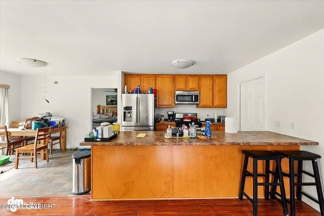 273 S Legacy Loop, Soldotna, AK 99669 - kitchen featuring stainless steel appliances, brown cabinetry, dark countertops, and a breakfast bar area
