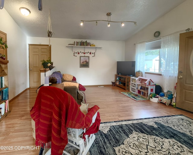 living room featuring wood finished floors, a textured ceiling, lofted ceiling, and baseboards