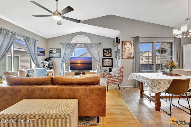 living area with vaulted ceiling, a ceiling fan, a chandelier, light wood-type flooring, and baseboards