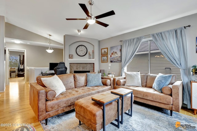 living area featuring ceiling fan, light wood-type flooring, a fireplace, and vaulted ceiling