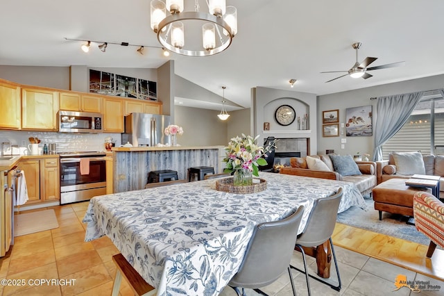 dining space featuring lofted ceiling, light tile patterned floors, a ceiling fan, a fireplace, and a chandelier