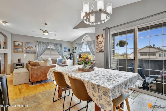 dining space with a ceiling fan, a chandelier, light tile patterned flooring, lofted ceiling, and a tiled fireplace