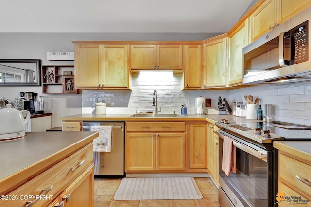 kitchen with appliances with stainless steel finishes, a sink, backsplash, light countertops, and light brown cabinetry