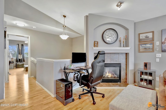 home office with light wood-style flooring, baseboards, a tile fireplace, and lofted ceiling