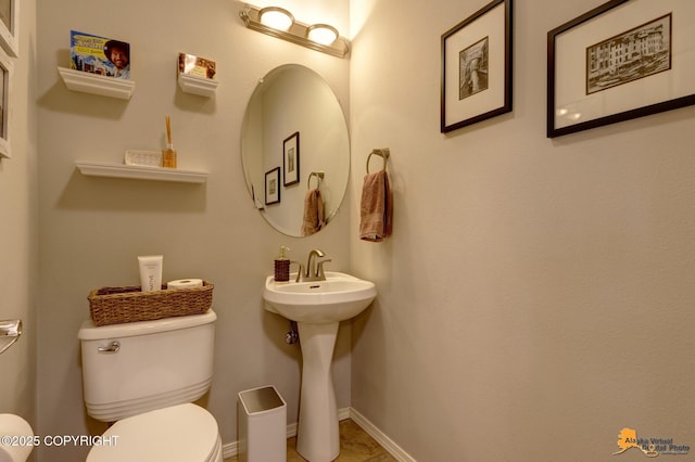 half bathroom featuring toilet, baseboards, and a sink
