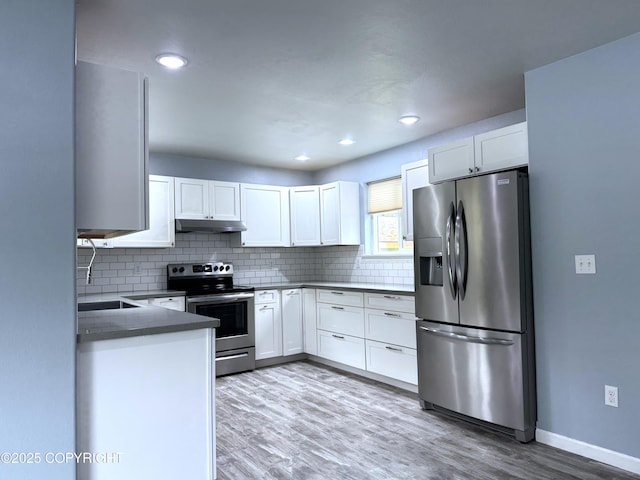 2321 Selief Ln, Kodiak, AK 99615 - kitchen featuring appliances with stainless steel finishes, under cabinet range hood, white cabinetry, decorative backsplash, and light wood-style flooring