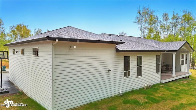 view of side of home featuring roof with shingles and a yard