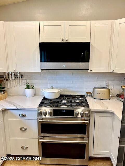 kitchen with range with two ovens, white cabinets, decorative backsplash, light stone countertops, and light wood-style flooring