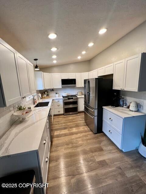 kitchen with stainless steel appliances, a sink, wood finished floors, recessed lighting, and white cabinetry