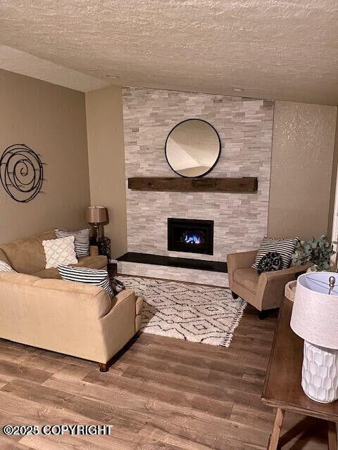 living area with wood finished floors, a textured ceiling, and a large fireplace